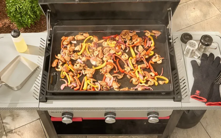 Weber Slate stekbord med svart lock och röd front mot tegelvägg, utomhusgrill med metallbas och kontroller.
